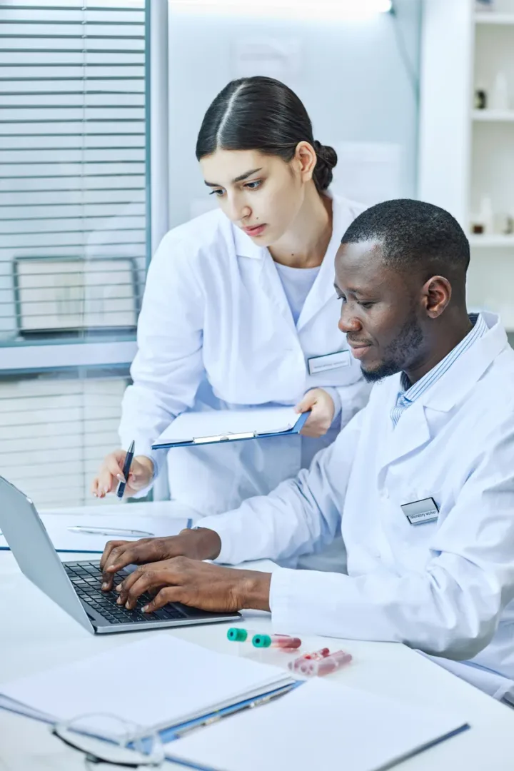 Vertical portrait of two scientists using laptop in medical laboratory