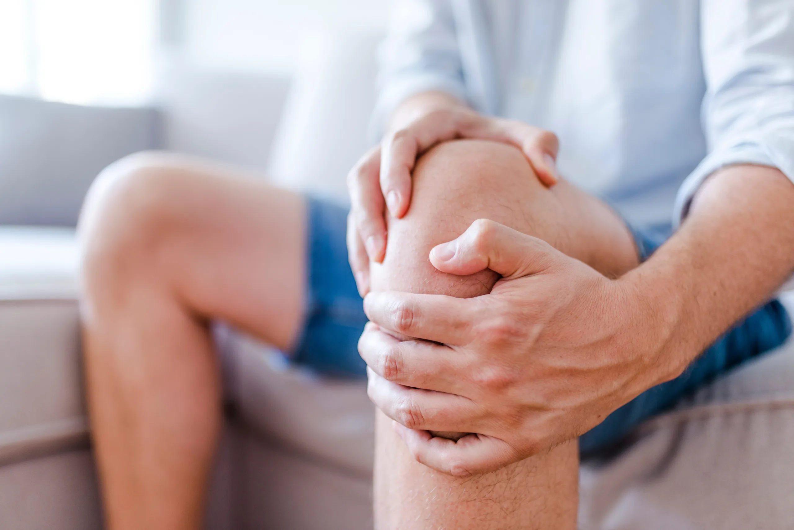 Man suffering from knee pain sitting sofa Man suffering from knee pain sitting sofa